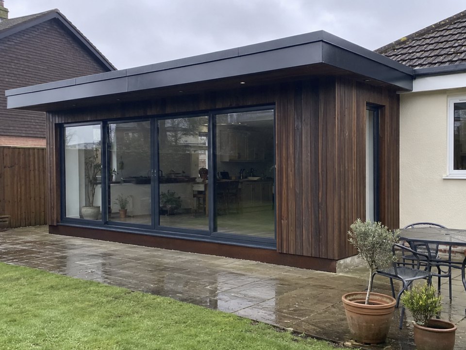 Timber clad garden room with full width sliding doors onto a patio